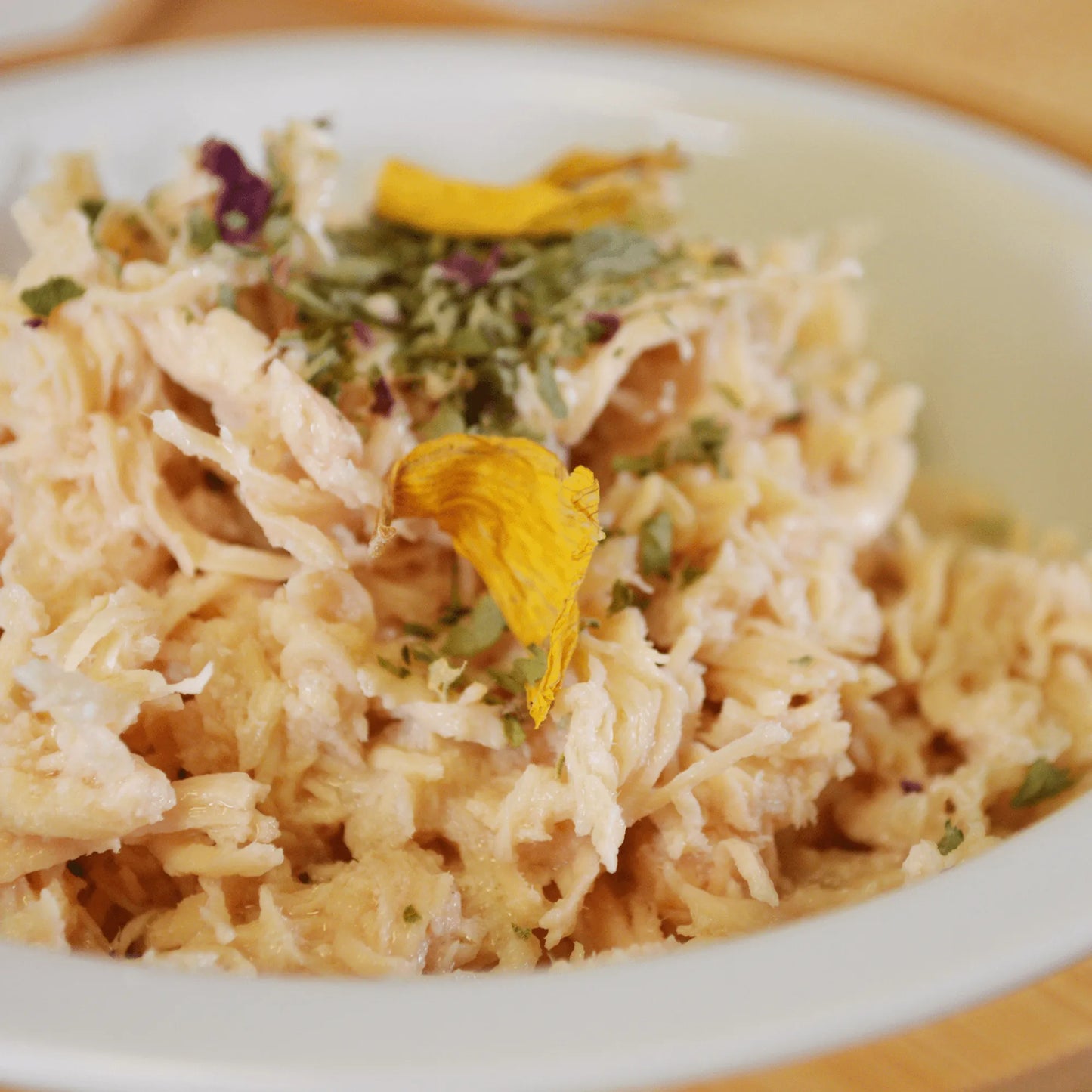 Close-up of shredded chicken topped with MJ's Rainbow Sprinkles, featuring herbs and flower petals.