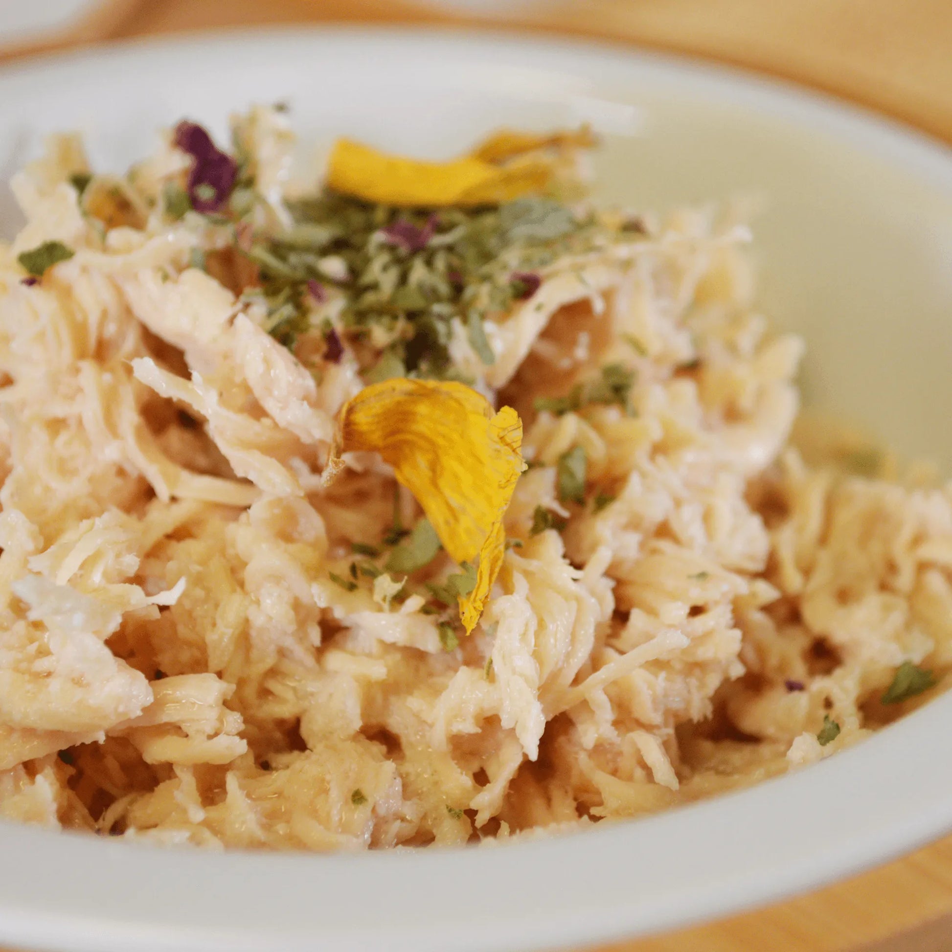 Close-up of shredded chicken topped with MJ's Rainbow Sprinkles, featuring herbs and flower petals.